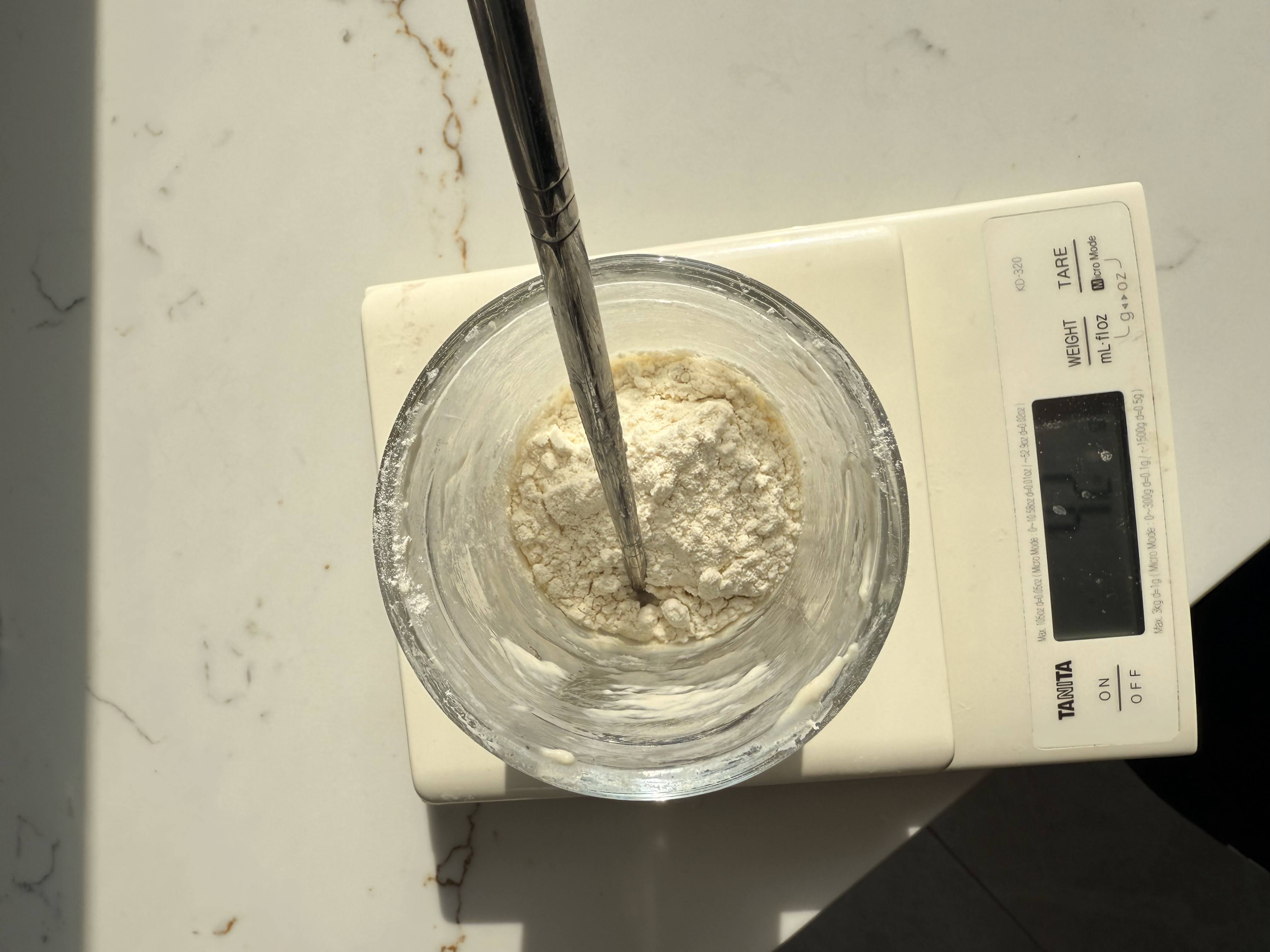 Adding flour to sourdough starter in a jar on a digital scale