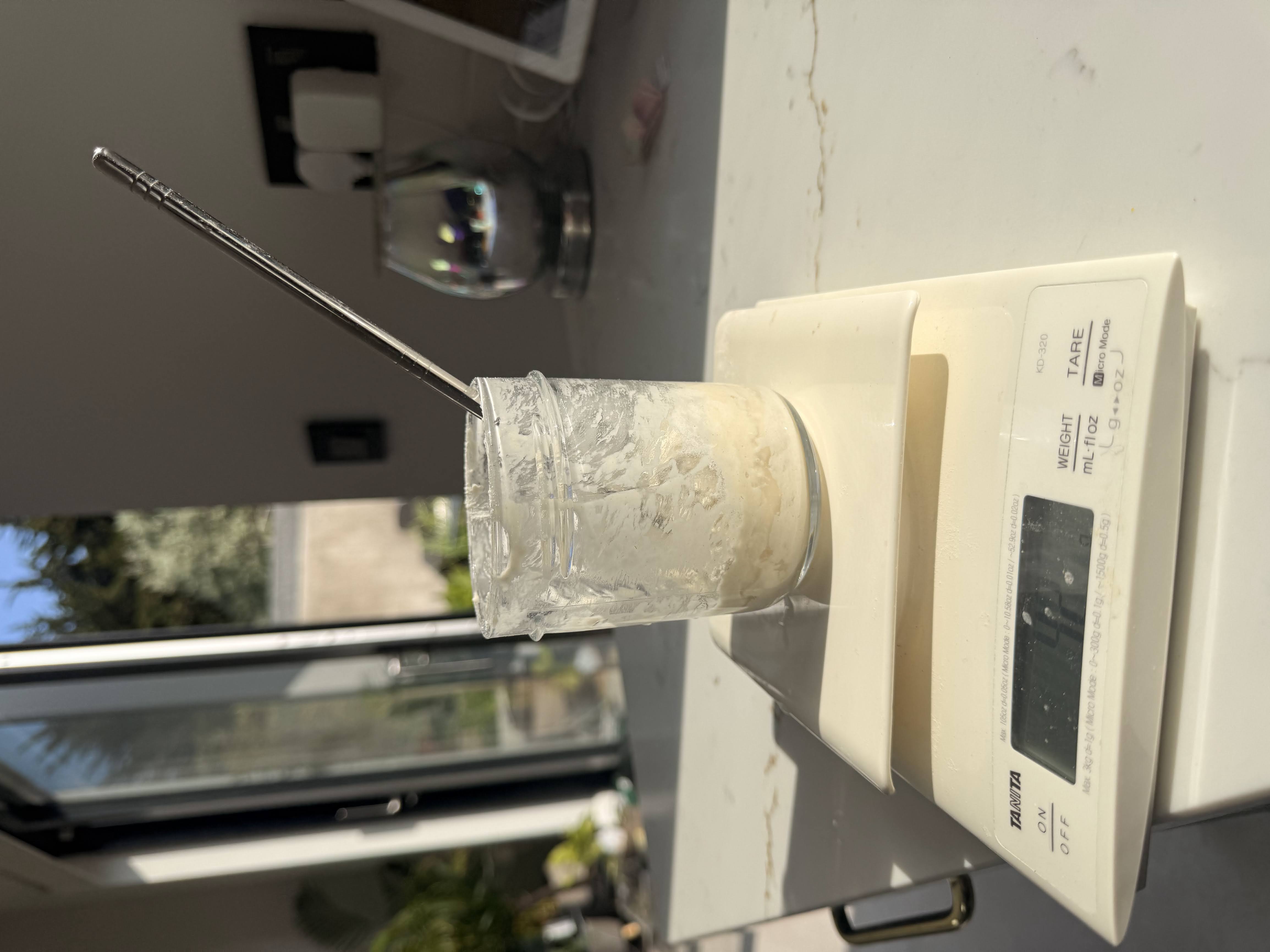 Sourdough starter in a jar on a scale, after water has been added to scrapings