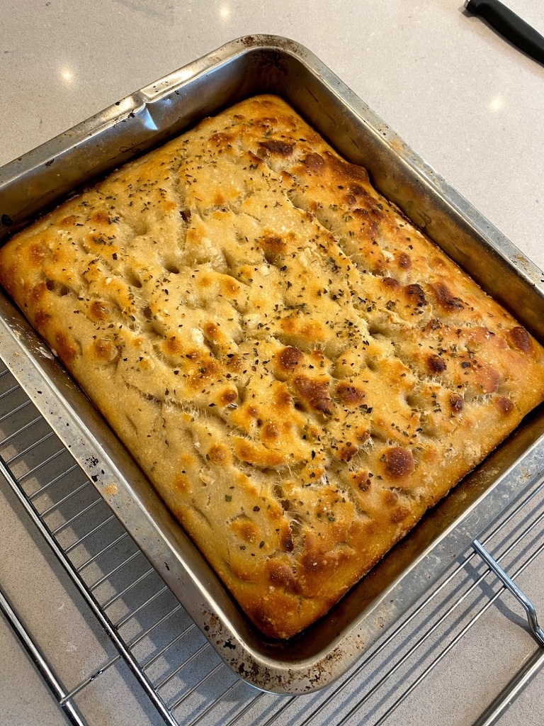 A freshly baked golden sourdough focaccia topped with rosemary and sea salt