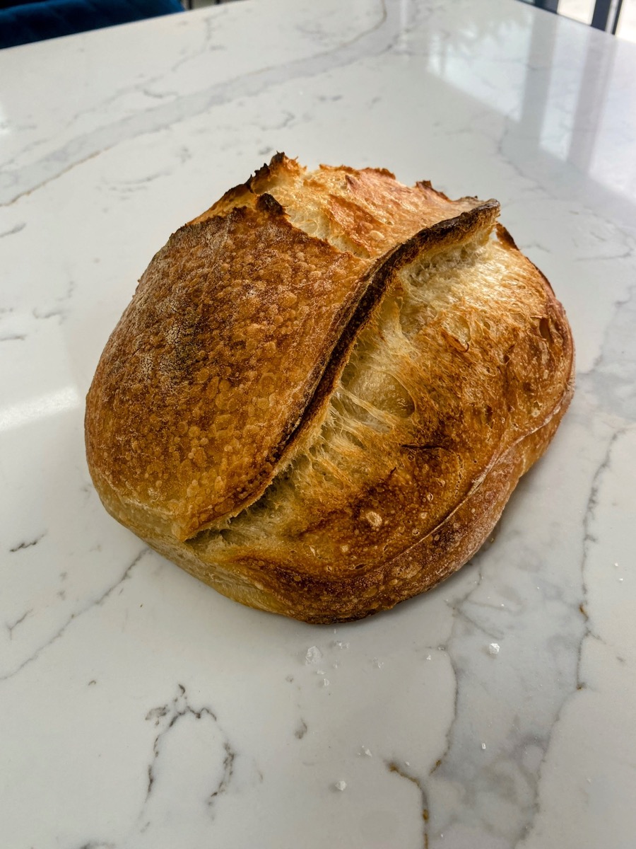 A freshly baked round sourdough loaf cooling on a wire rack